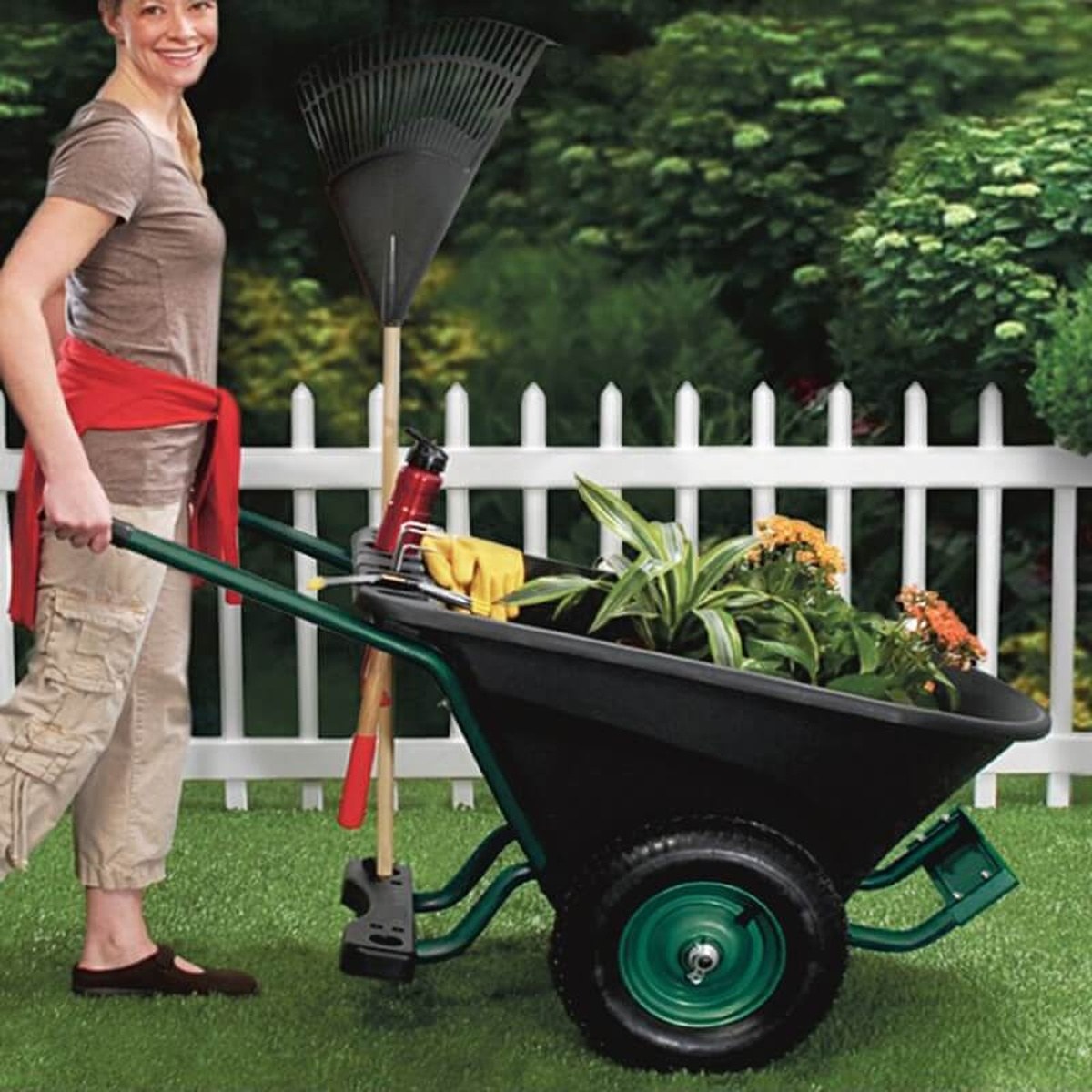 Kvinde med trillebør, fyldt med planter og haveredskaber, i haven